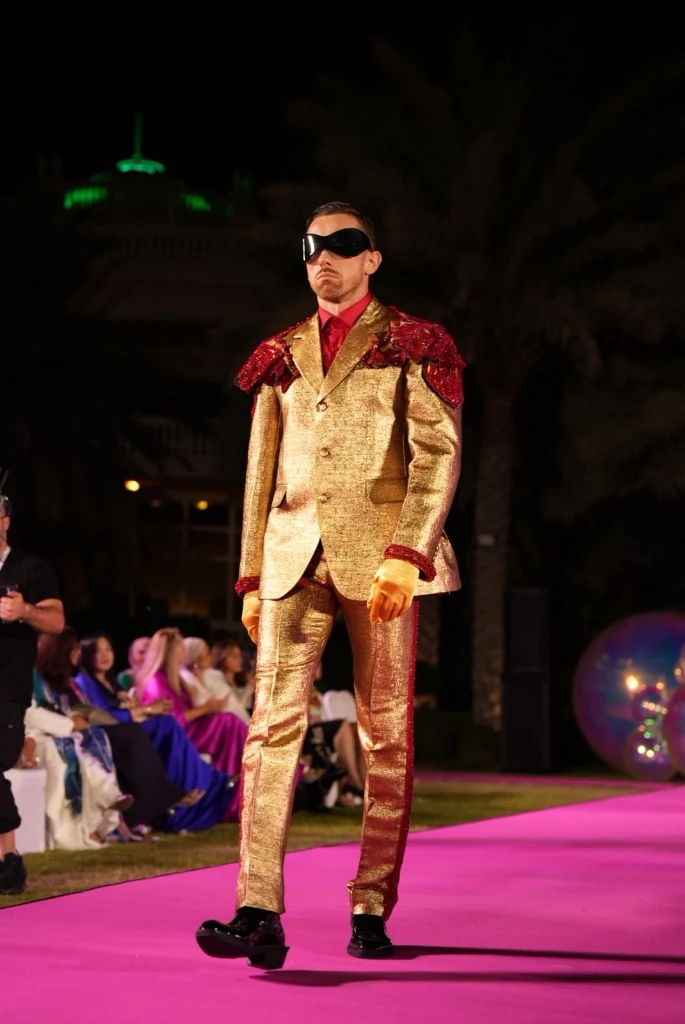 Modelo de terno dourado com ombreiras vermelhas e máscara na passarela