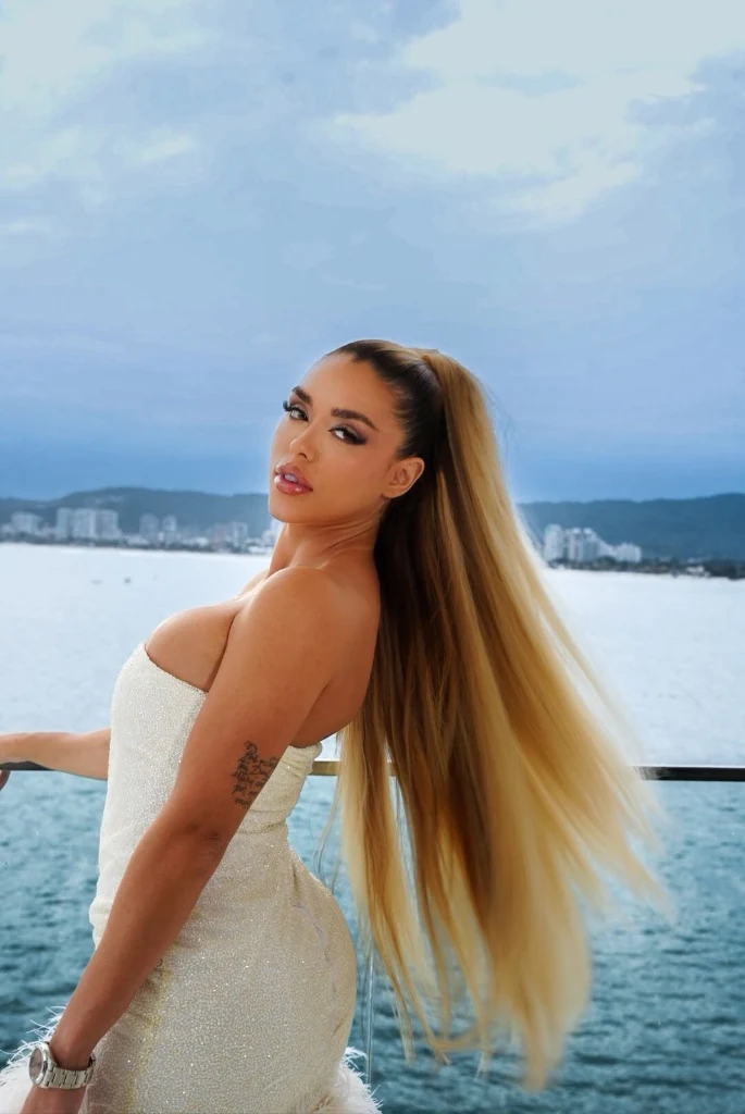 Modelo de vestido branco e cabelo longo, com o mar e a cidade ao fundo